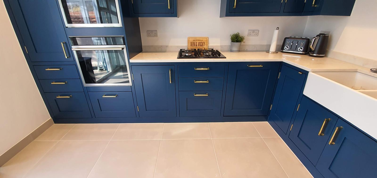 Modern blue kitchen with brass handles and beige floor tiles